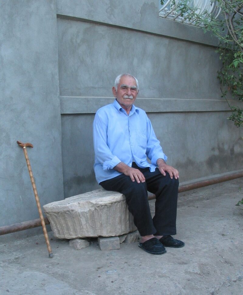 Das große Bruchstück einer Glockenbasis diente Hamid Jussibov viele Jahre als Sitzplatz vor seinem Haus in Karačamirli, 2006 (Foto: G. Mehnert) ein älterer Herr sitzt auf einem Steinsockel